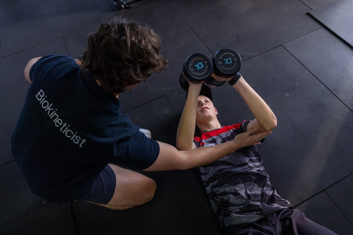 The academy biokineticist coaching a rider through a dumbbell press